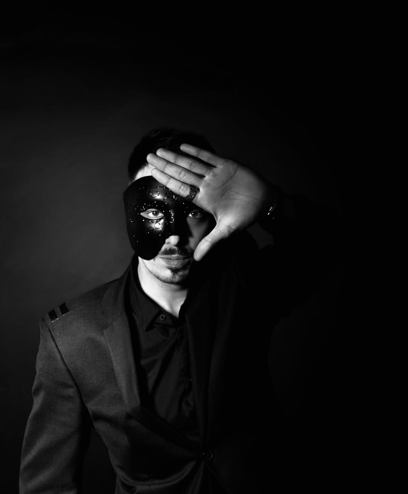 Mężczyzna w czarnej masce odsłaniający jedno oko dłonią – symbol obnażania marketingowych iluzji